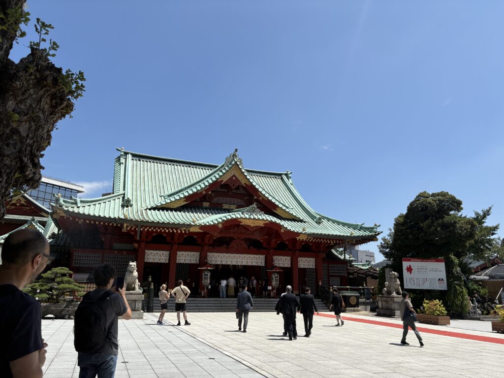 青空の下に建つ神田明神の社殿と参拝する人たち